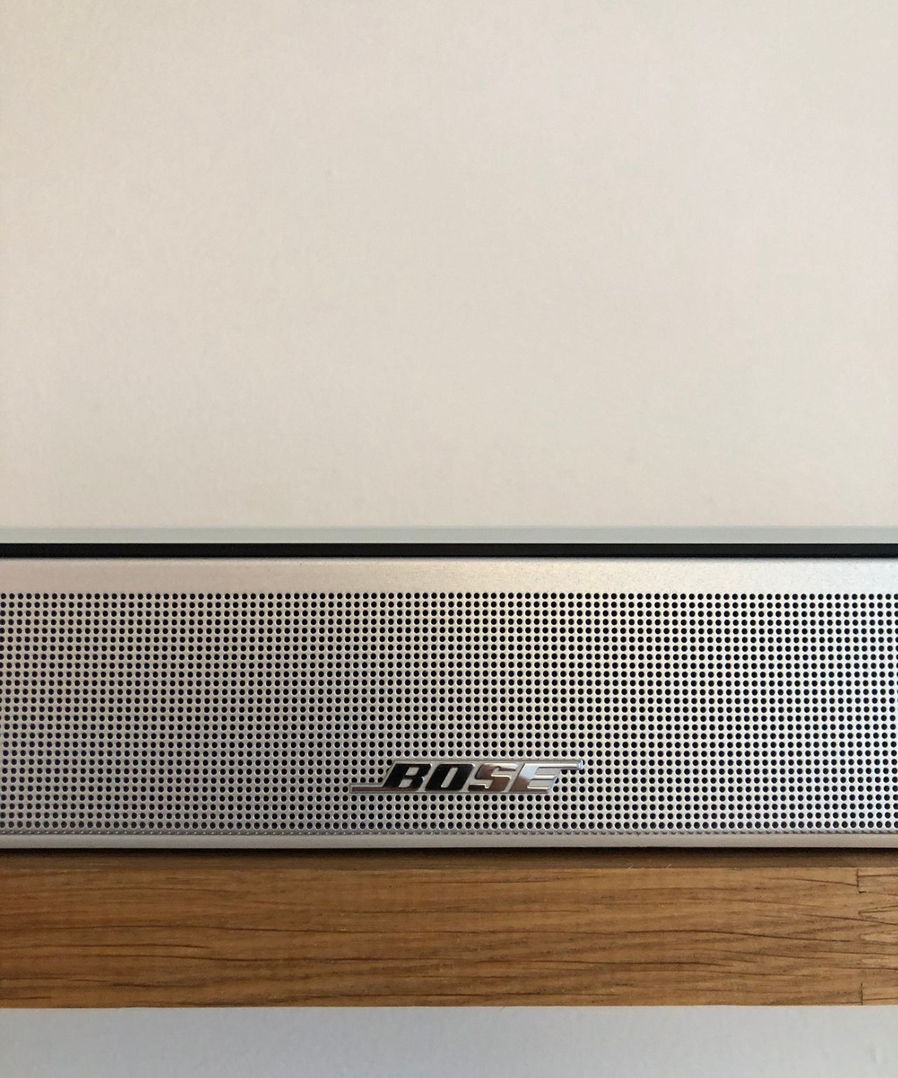 Closeup of the Bose Smart Ultra Soundbar on wooden shelf in front of white wall in Dan Fauzi's home.