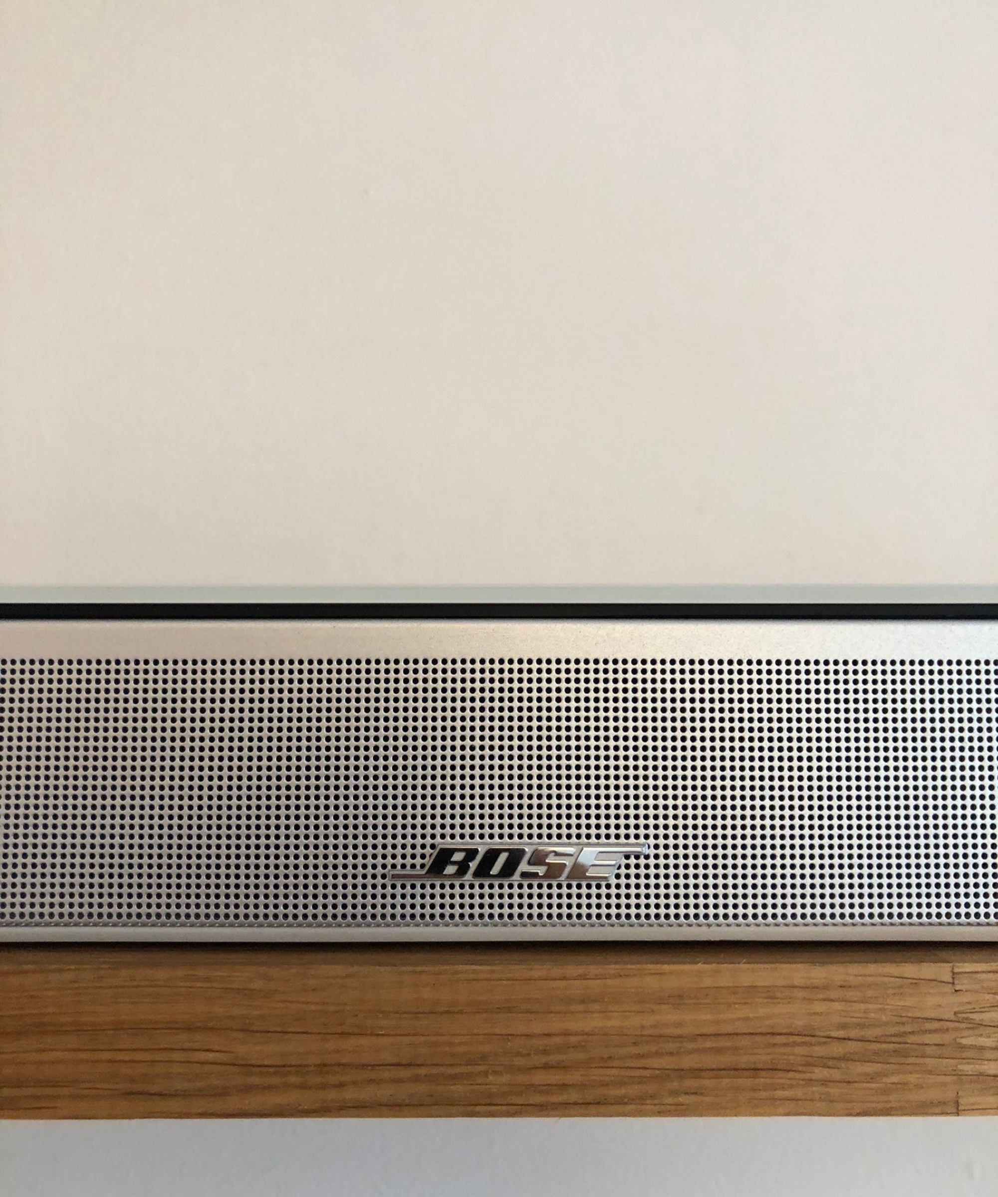 Closeup of the Bose Smart Ultra Soundbar on wooden shelf in front of white wall in Dan Fauzi's home.