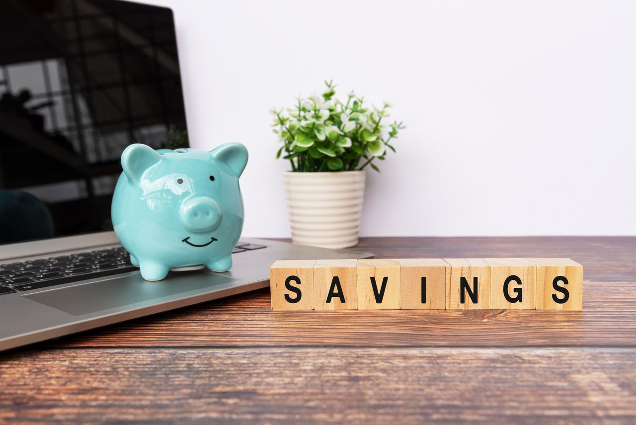 Blue piggy bank sitting on top of laptop on a desk with the word savings spelled out in wooden blocks