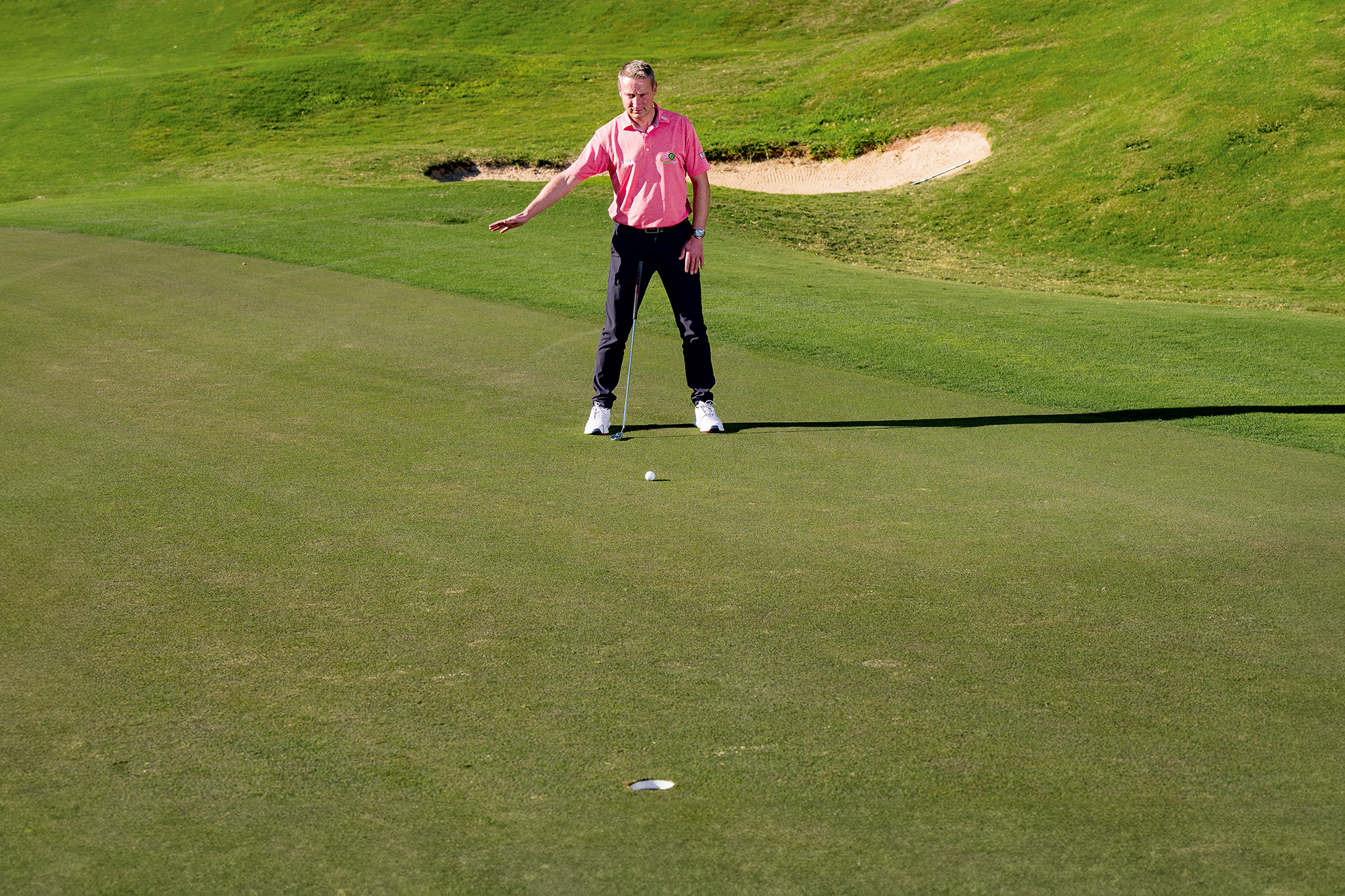Anders Mankert demonstrating that the putt is moving from left to right by reading from below the hole using his feet and eyes, signalling with his right arm that the putt will travel right