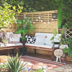 A garden with two outdoor benches with cream cushions in a boho-themed corner