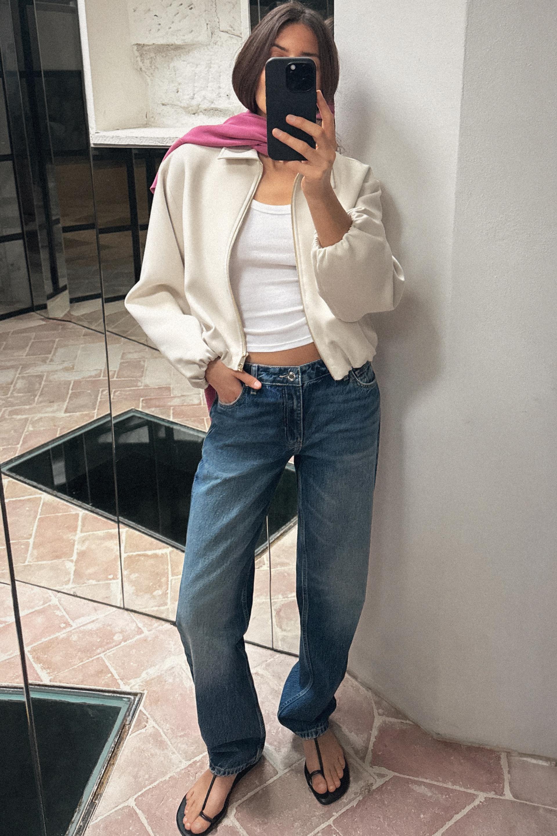 Zara model posing for a mirror selfie wearing a pink scarf, white cropped jacket, a white tank top, straight-leg jeans, and black toe-wrap sandals.