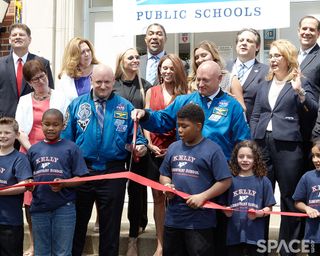 Children hold a red ribbon as Mark and Scott Kelly wield giant scissors