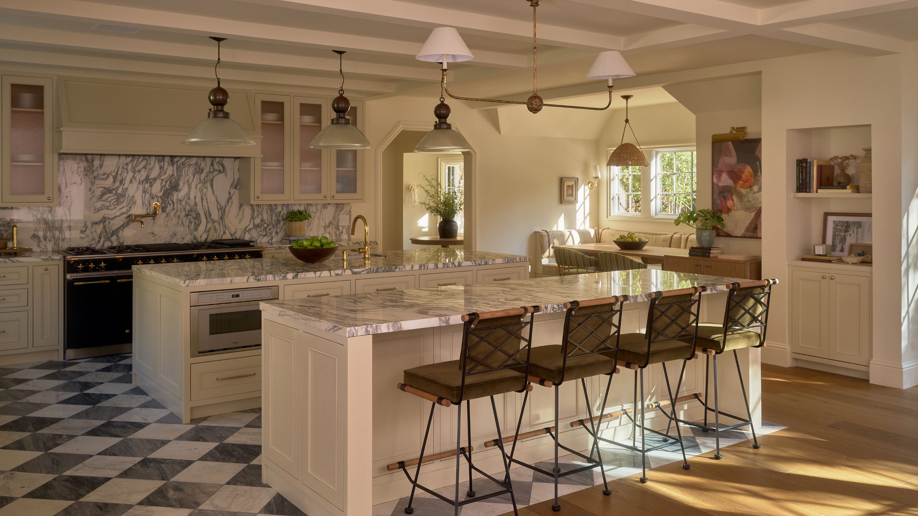 a large LA open plan kitchen with checkerboard tiled floor, neutral cabinets, large range cooker,island with metal stools, and a tucked away dining nook