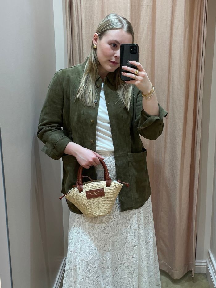 Woman wears green shirt, white T-shirt, white skirt and carries basket bag from Sezane