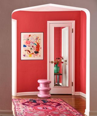 entryway with bright red wall, white trim and pink patterned rug