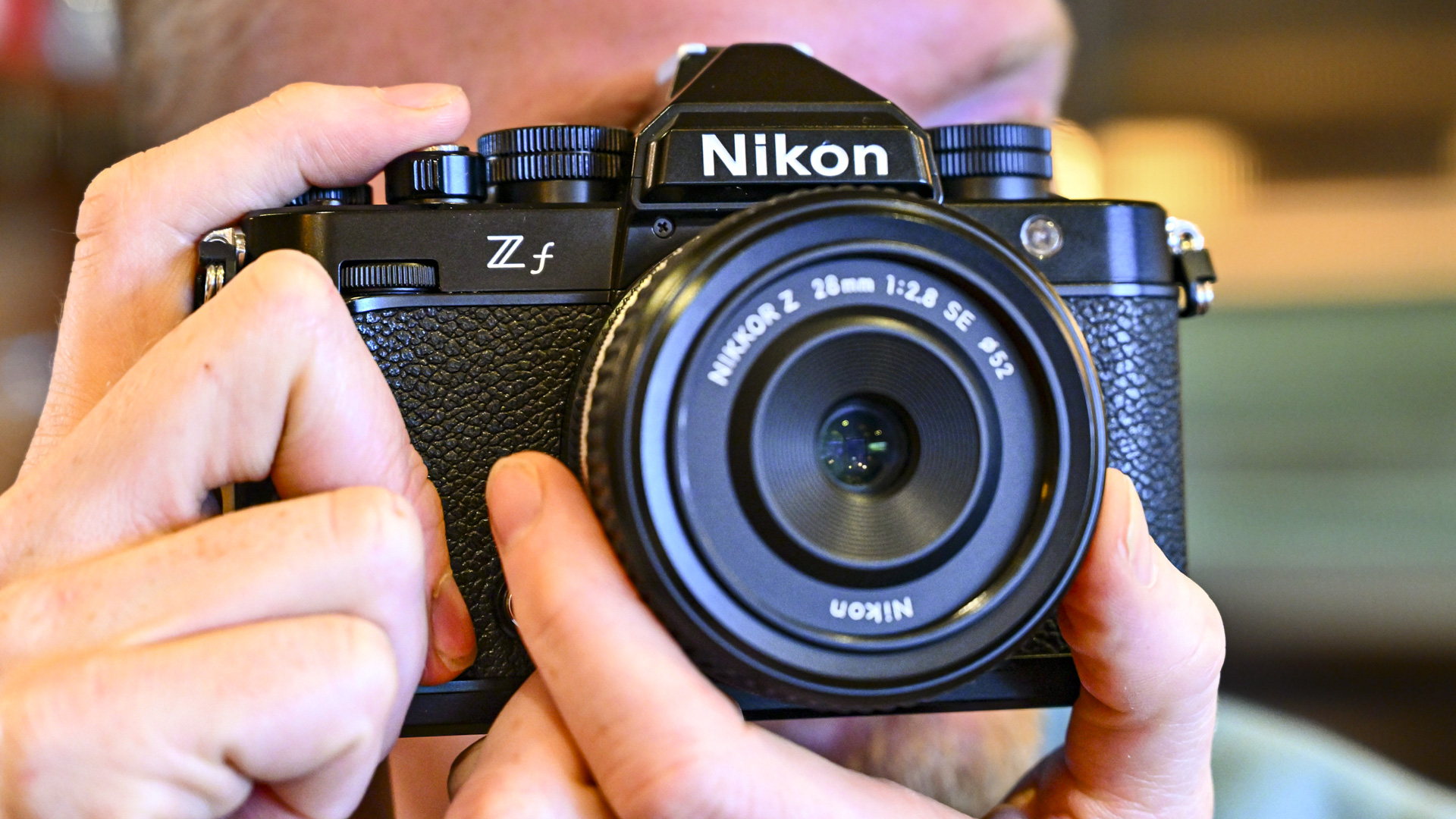 Appareil photo Nikon Zf tenu devant l'œil du photographe utilisant le viseur, avec l'objectif Z 28mm F2.8 SE monté
