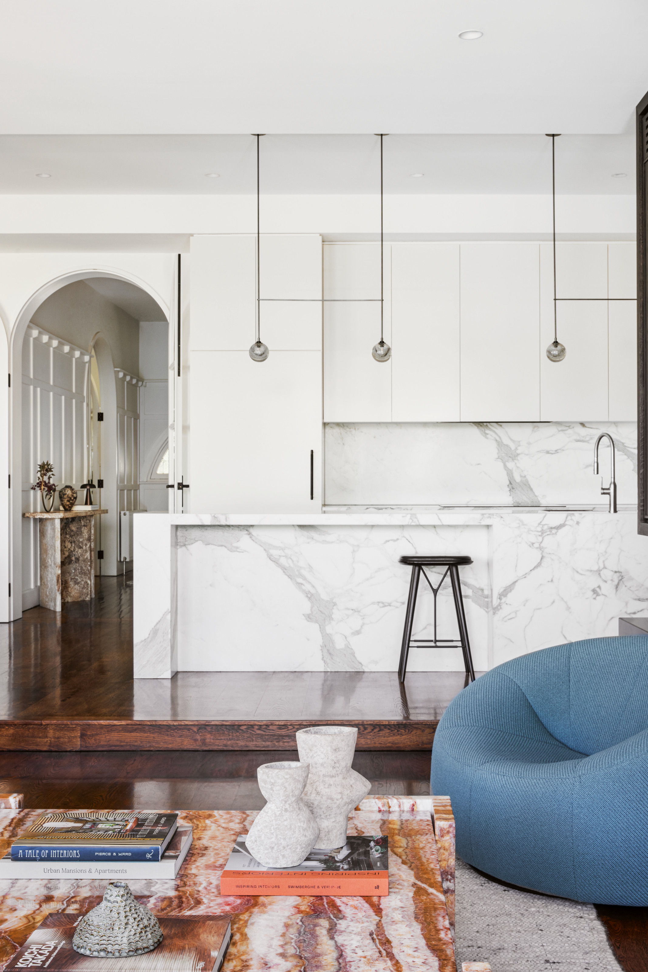 White kitchen with marble island, a comfy blue chair and marble coffee table are in front
