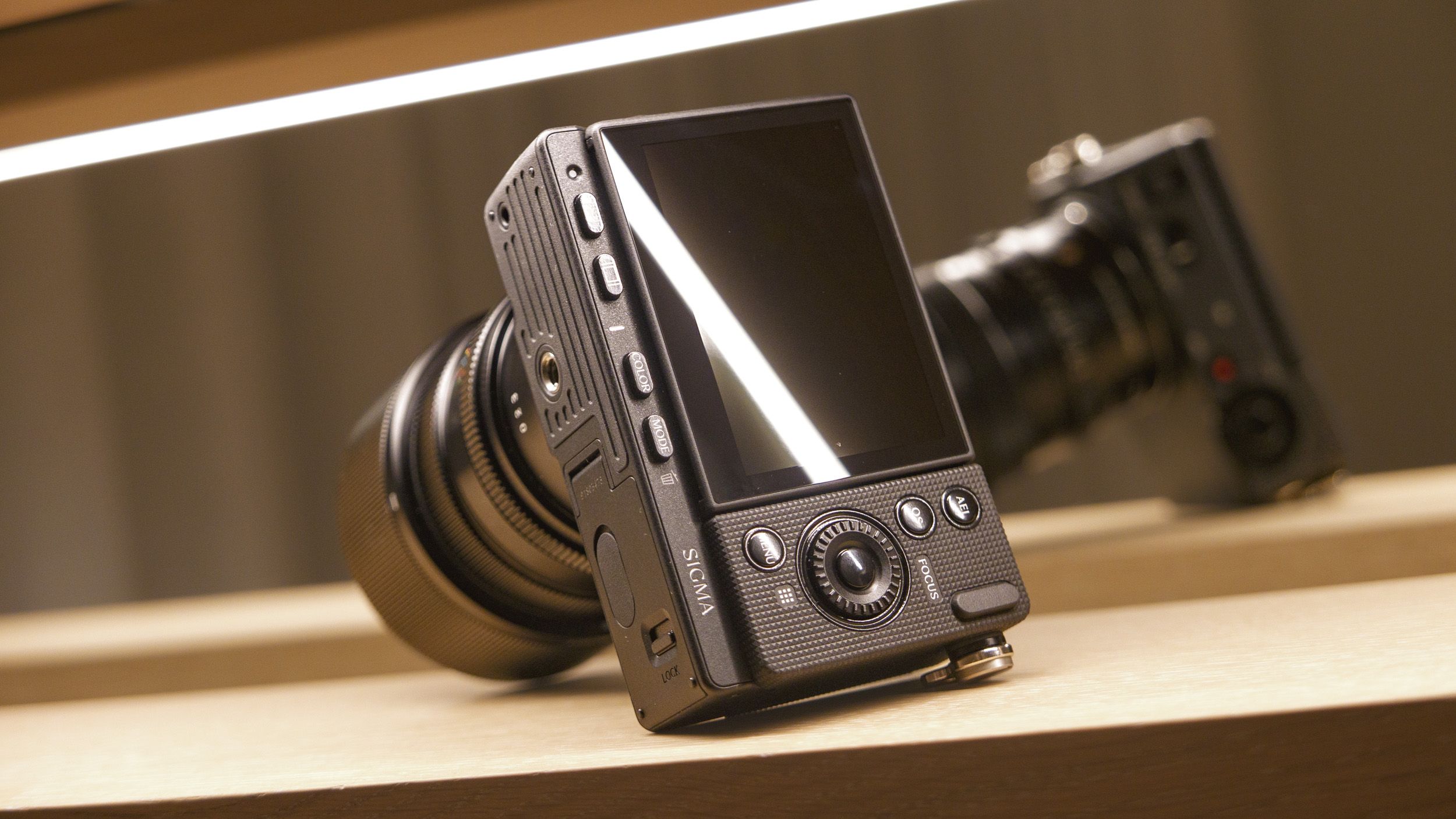 Sigma FP2 mirrorless camera with 50mm f/2 contemporary lenses attached, on a shelf, lit from above, view of its back