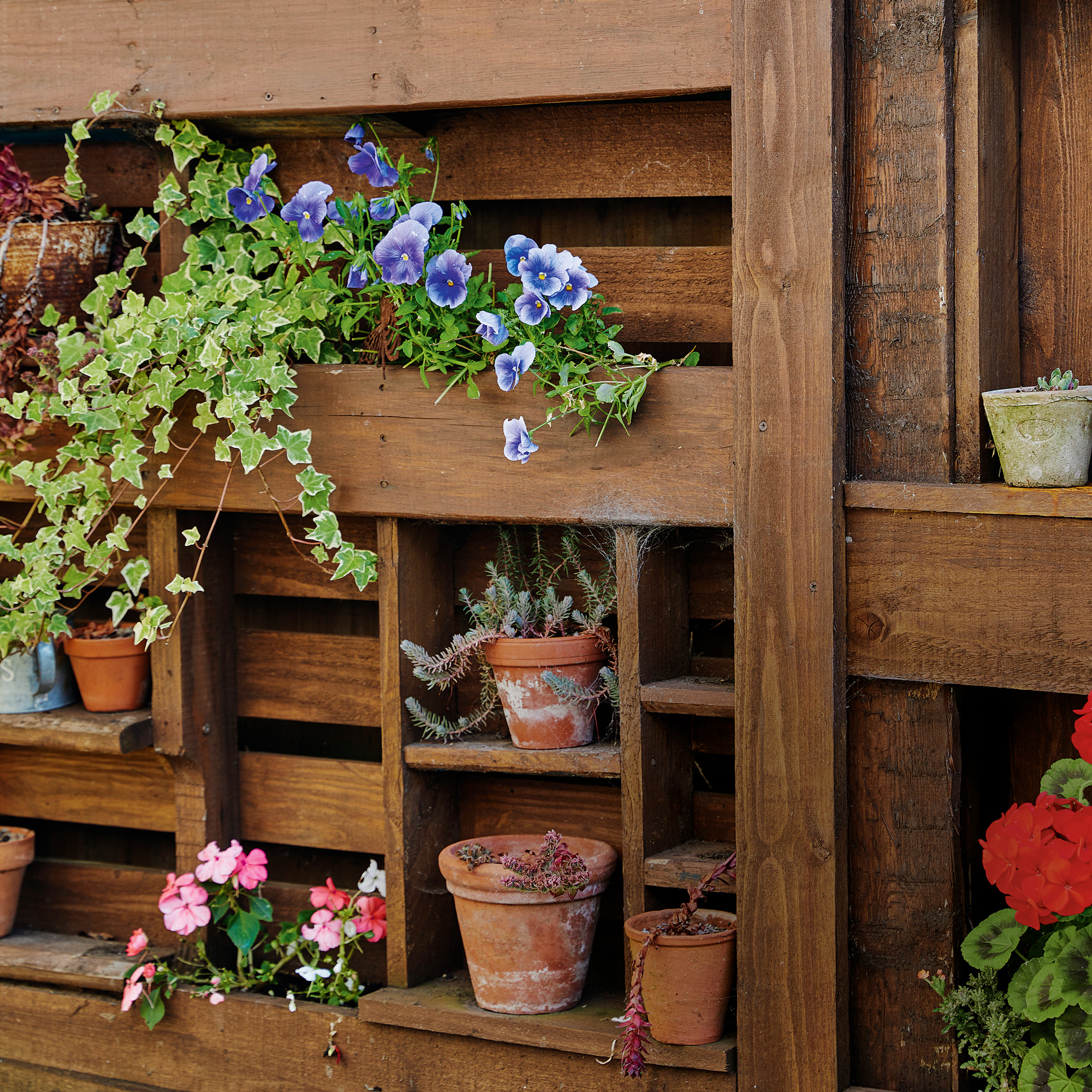 a close up of a vertical shelving storage unit in a garden filled with planters and flowers