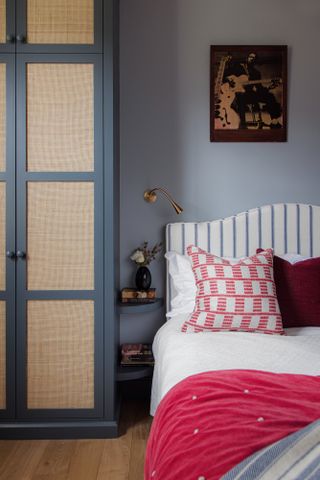 Bedroom with blue painted walls, built-in wardrobe with cane inset, striped headboard and bright pink throw and cushion