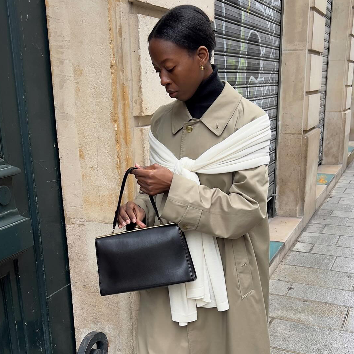 French woman wearing cotton khaki trench coat with white sweater draped across her shoulders.