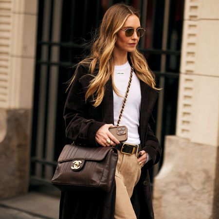 Fashion week attendee wearing sunglasses, white shirt, long coat, and brown chanel crossbody bag 