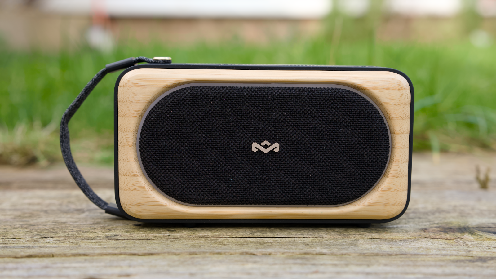 House of Marley Roots Solar Bluetooth speaker outdoors in a garden, on a wooden bench.
