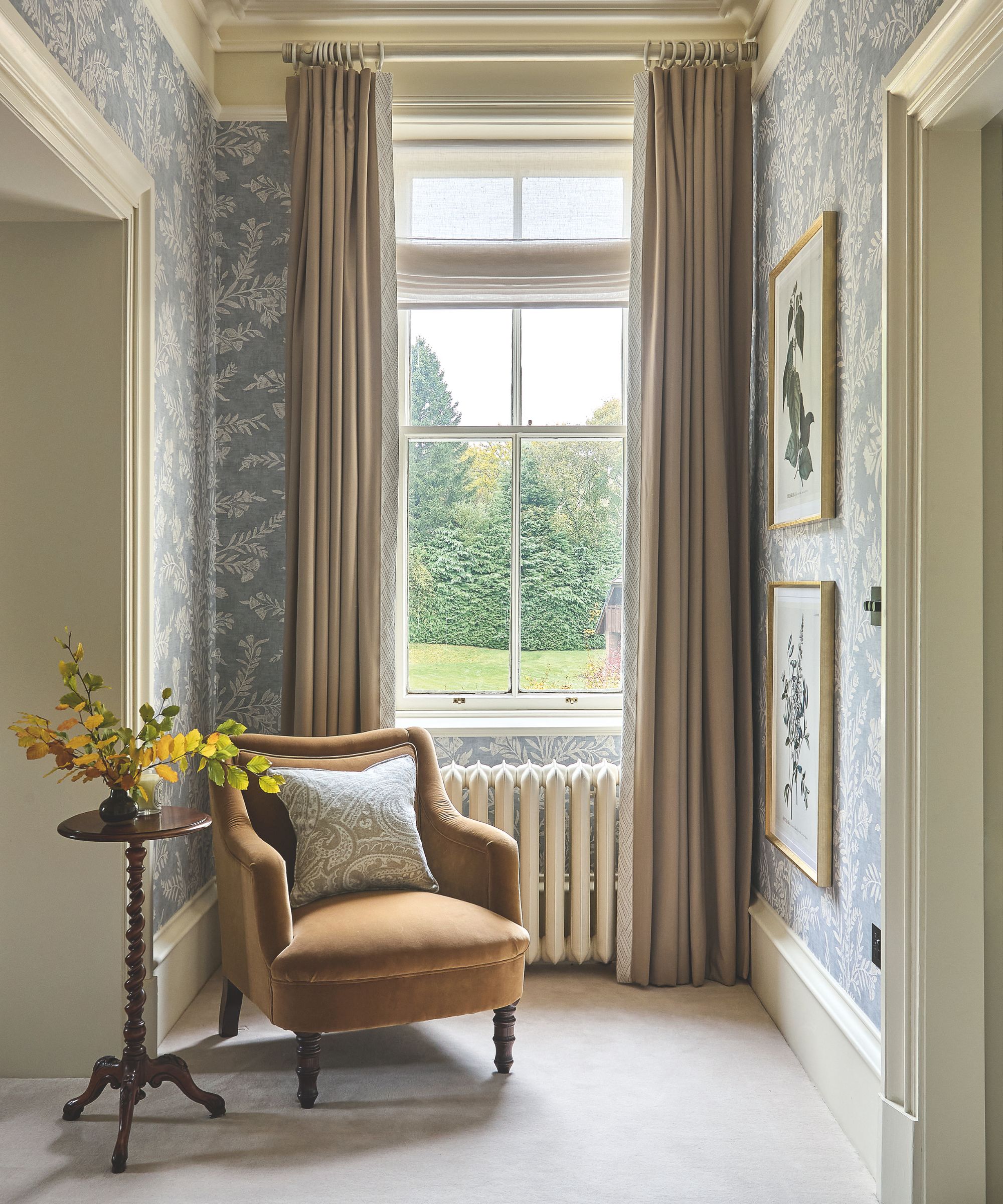Entryway with large window with beige curtains, blue and white floral wallpaper, orange chair and small wooden side table