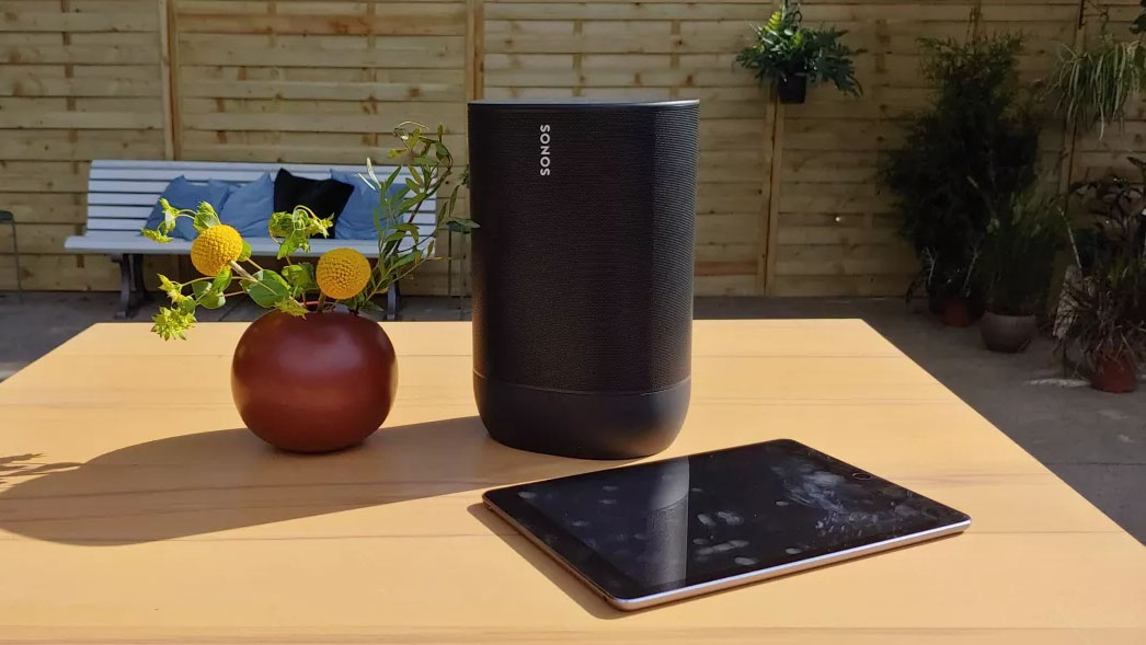 The Sonos Move speaker in black pictured outside on a wooden table next to a tablet