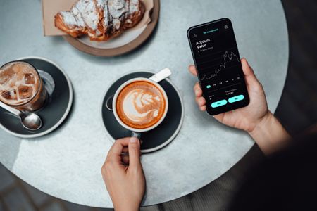 woman checking the stock market on smartphone, having breakfast at coffee shop