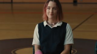 Saoirse Ronan smiling in a gym wearing a blue sweater over a white top