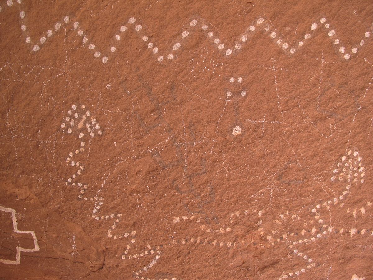 The same sandstone rock panel in natural colour, showing faint white dotted zigzag patterns and geometric markings against a weathered red-brown surface.