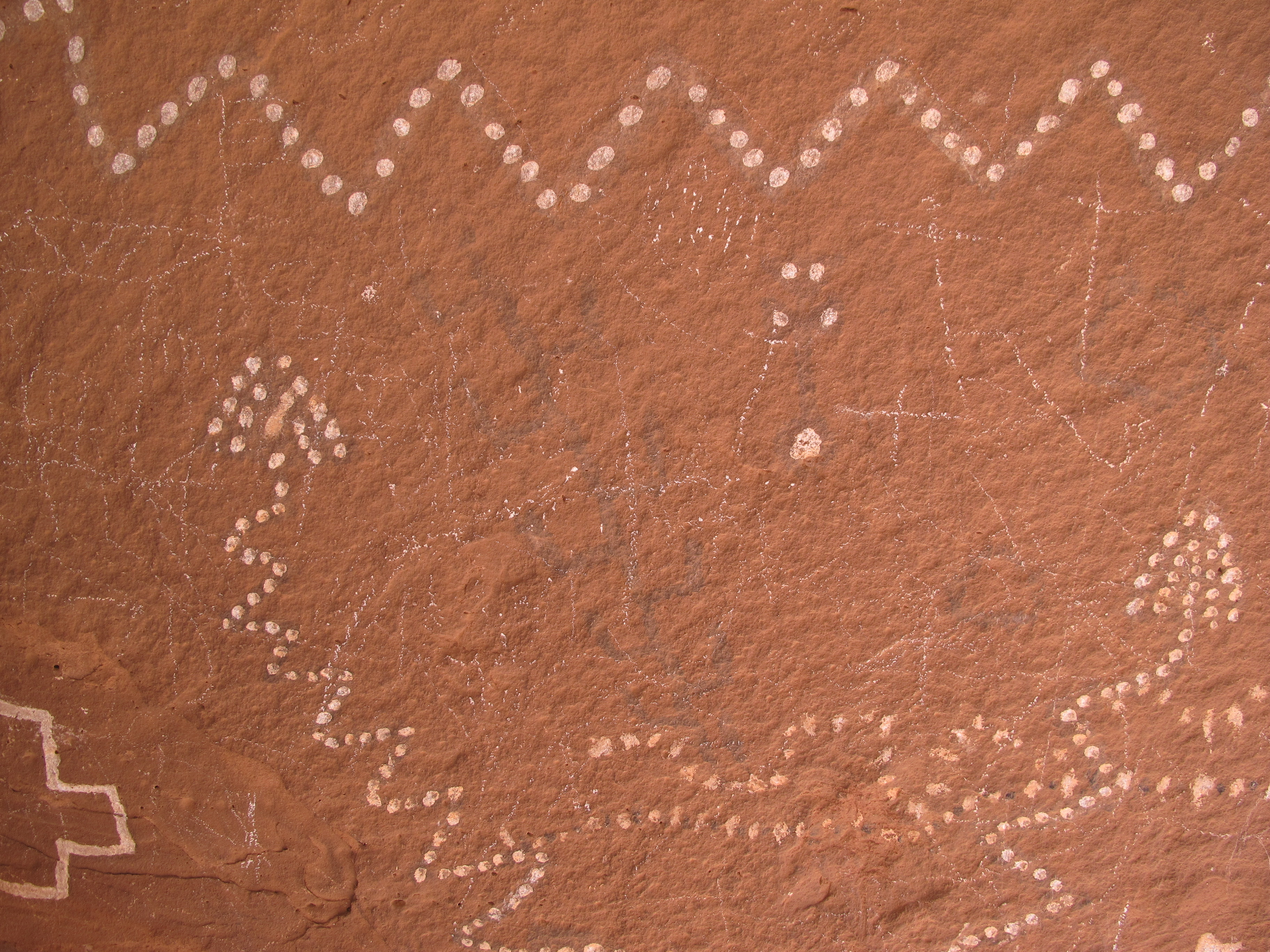 The same sandstone rock panel in natural colour, showing faint white dotted zigzag patterns and geometric markings against a weathered red-brown surface.