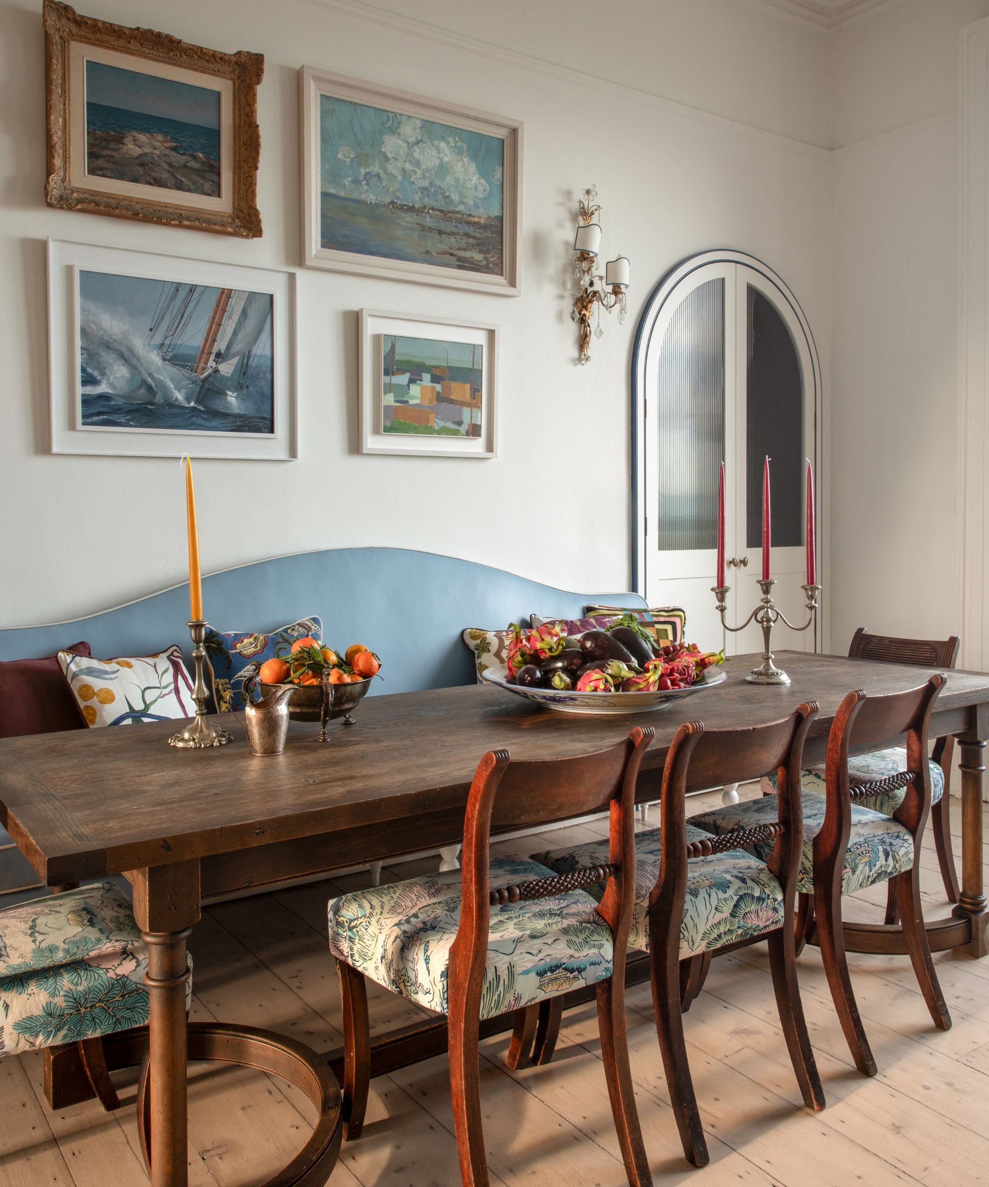 a white painted kitchen with a dining nook, a dark wooden antique table and chairs with a blue upholstered banquette and vintage art