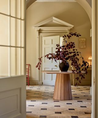 tiled entryway with a wooden large round table with a dark red foliage display