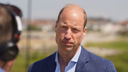 Prince William looking serious wearing a blue suit jacket outside 