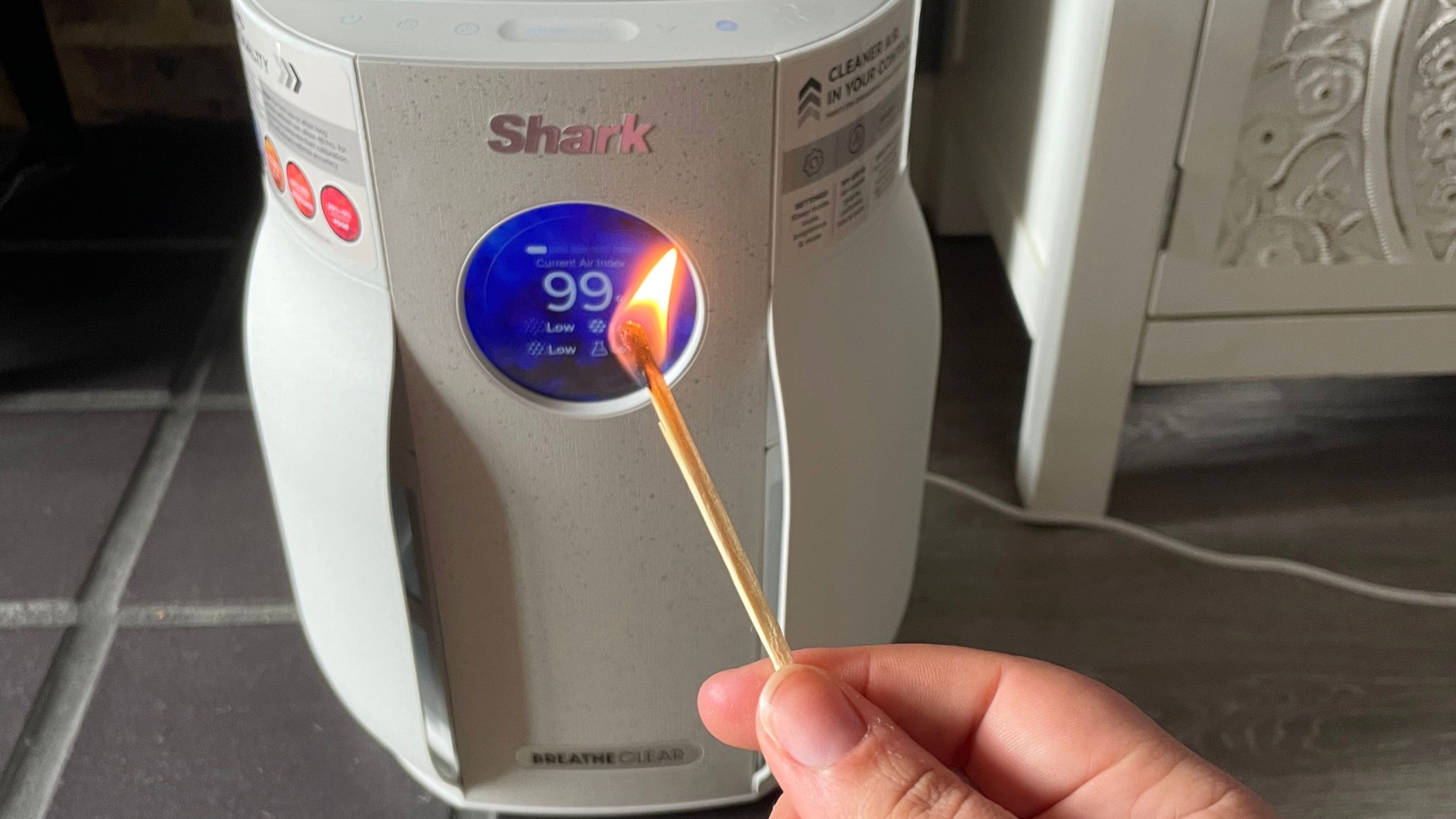 Hand holding a lit match in front of the Shark BreatheClear Compact Air Purifier with NeverChange6
