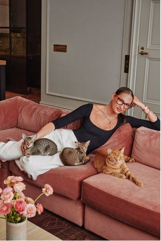 Jenna Lyons sitting on a pink velvet vouch with three cats