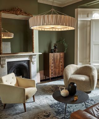 Cozy living room with seating zone, low hanging oversized pendant, green painted walls, fireplace, neutral and natural furniture