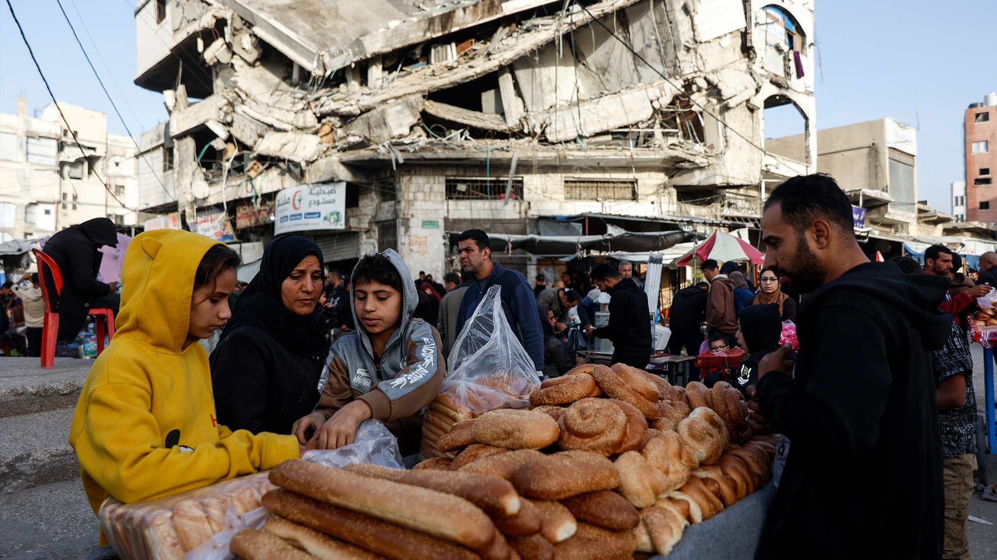 Palestinians sell bread on a street beneath a destroyed building in Zawiya market, Gaza City, Palestine