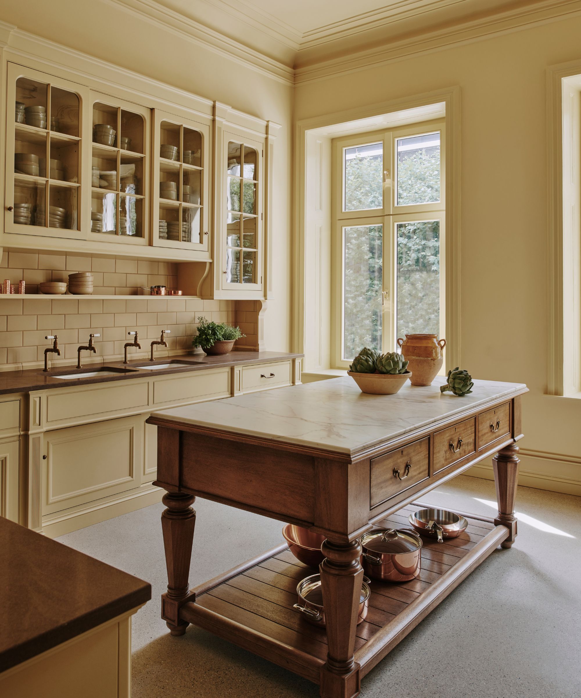 Farmhouse style kitchen with wood table island, glass cabinets painted butter yellow and sink with wood countertop