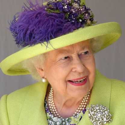 Queen Elizabeth wearing a lime green and purple hat and coat with a diamond brooch smiling and looking to the right