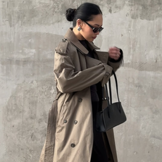 Dawn Tan wearing a tan trench coach with a black bag and black sunglasses.