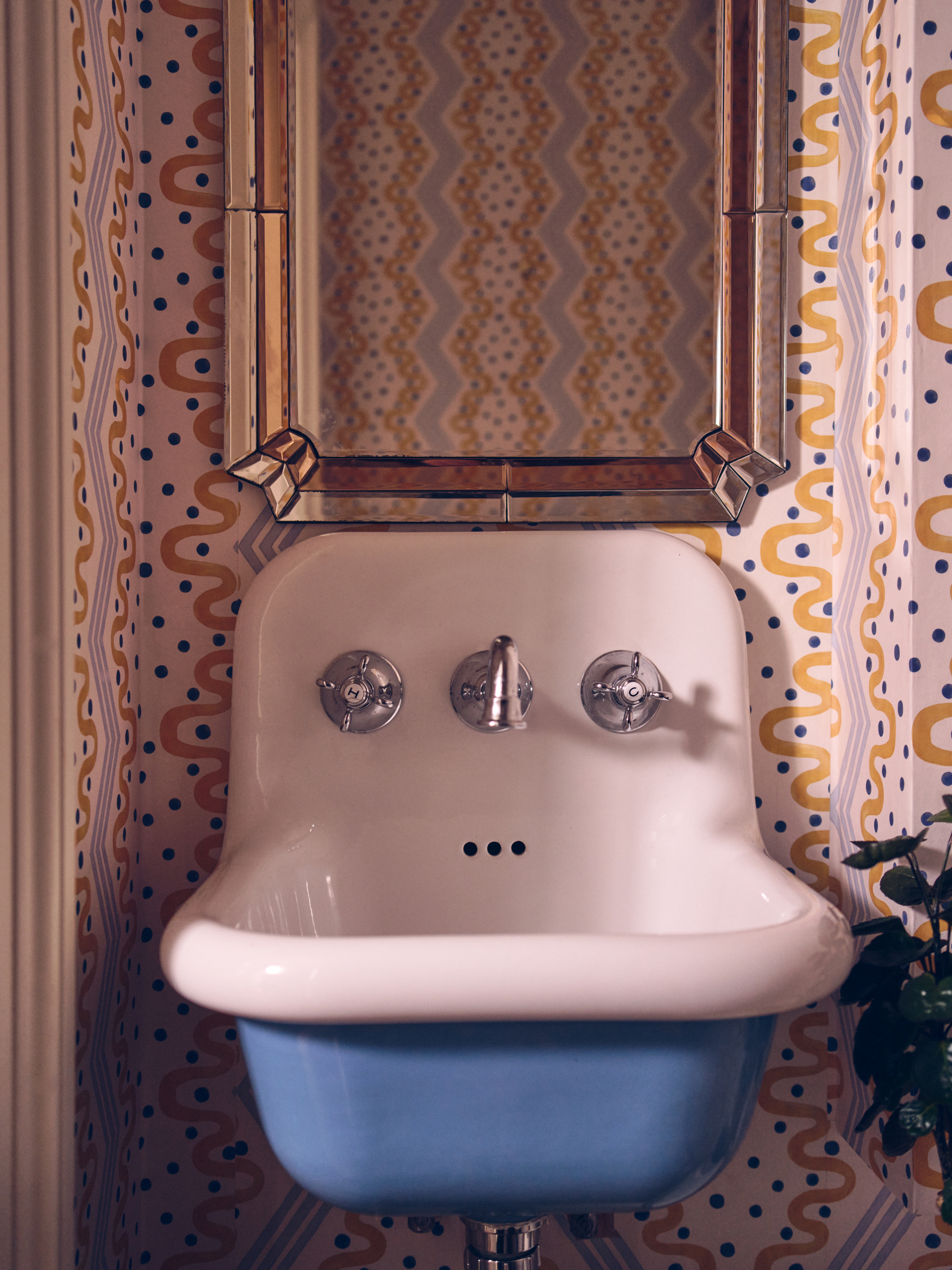 small bathroom sink with patterned wallpaper and gold mirror