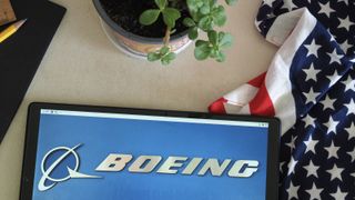The Boeing logo on an tablet on a desk with a US flag and plant pot