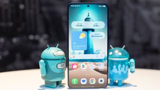 Samsung Galaxy S25 Plus in Navy Blue showing home screen with AI generated lighthouse, standinng in between two adorable Android figurines