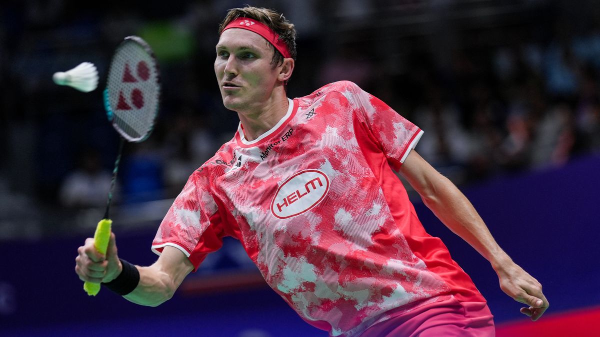 Viktor Axelsen of Denmark plays a shot in his red and white t-shirt and red headband.