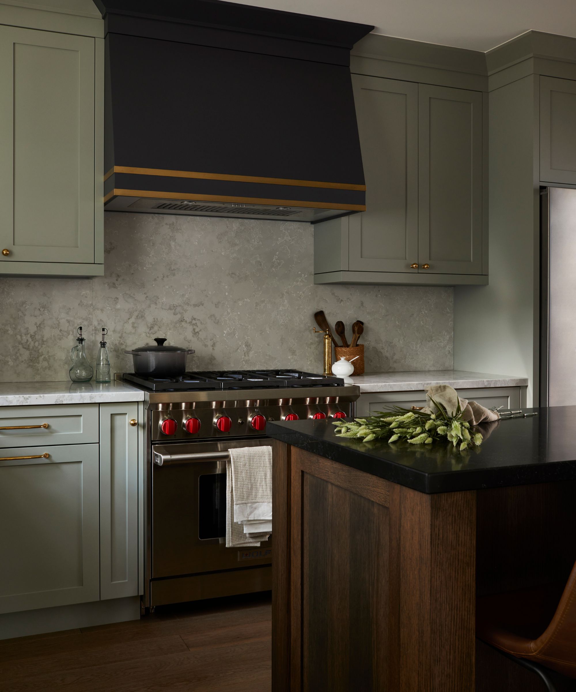 a warm sage green kitchen with a dark custom cooker hood, stainless steel stove, and a wooden kitchen island