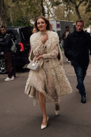 woman wearing sleeveless faux fur coat, sheer dress, and heels