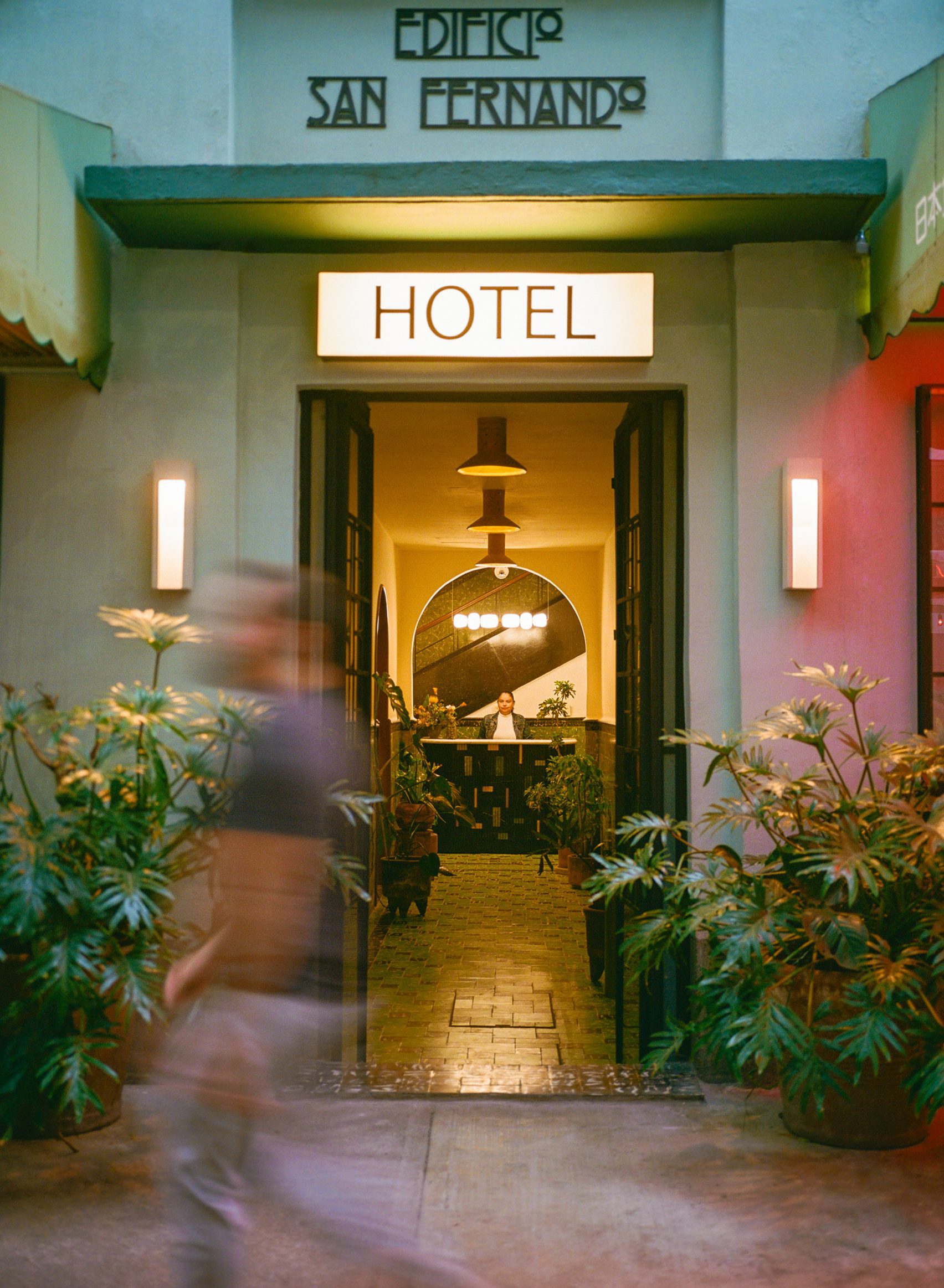 A vibrantly decorated hotel boasts a welcoming palette of pastel greens, pinks, and browns, softly glowing lighting, and a retro-fueled energy.