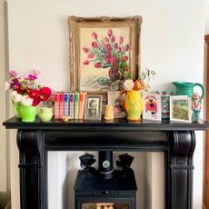 Fireplace mantlepiece with colourful books, vases filled with flowers and floral painting