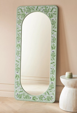 floral green floor mirror leaning against a wall