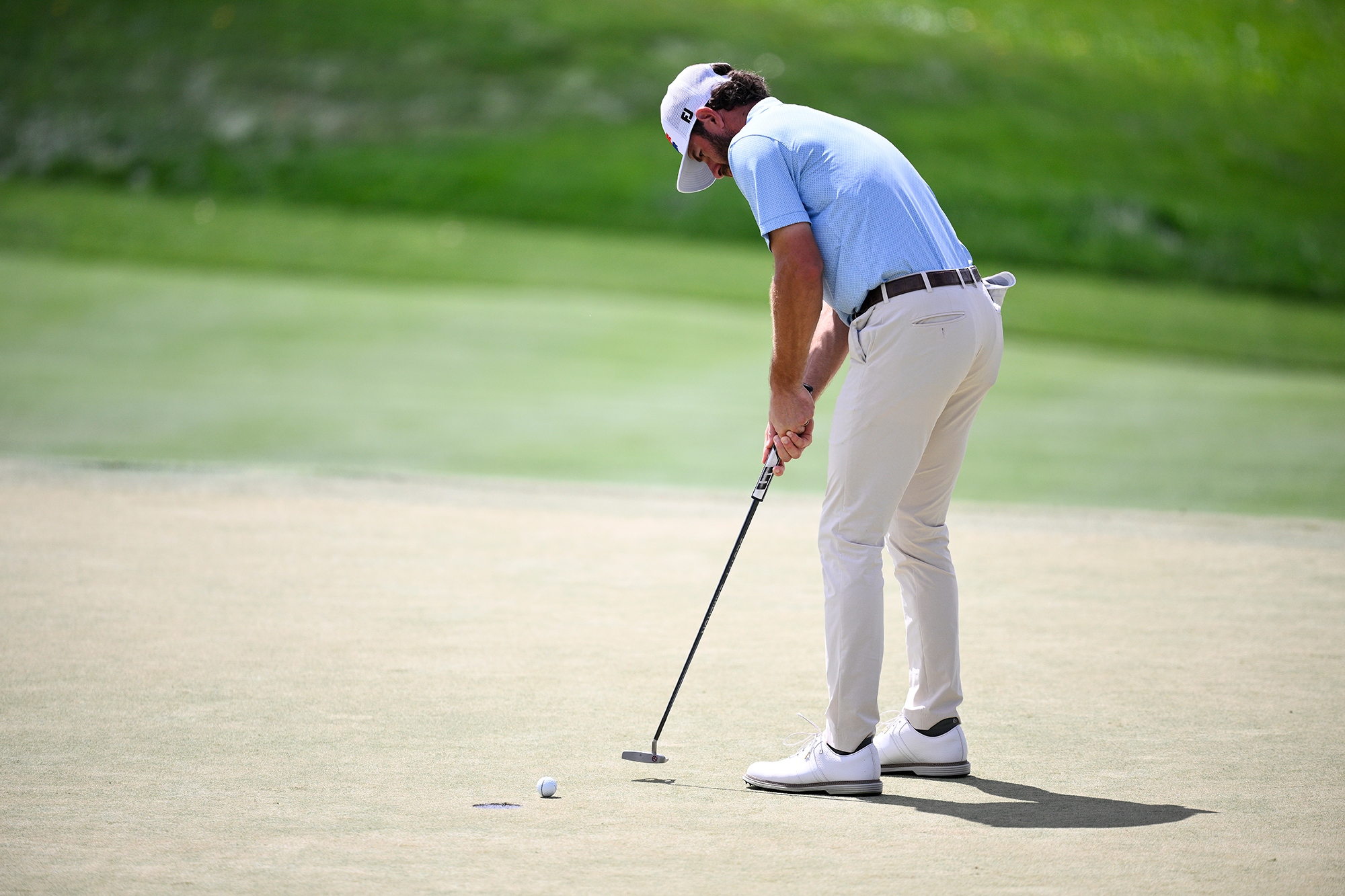 Cameron Young hitting a short putt on the green, with his golf ball about to drop into the hole