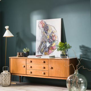 Green living room with low mid-century sideboard, artwork and floor lamp