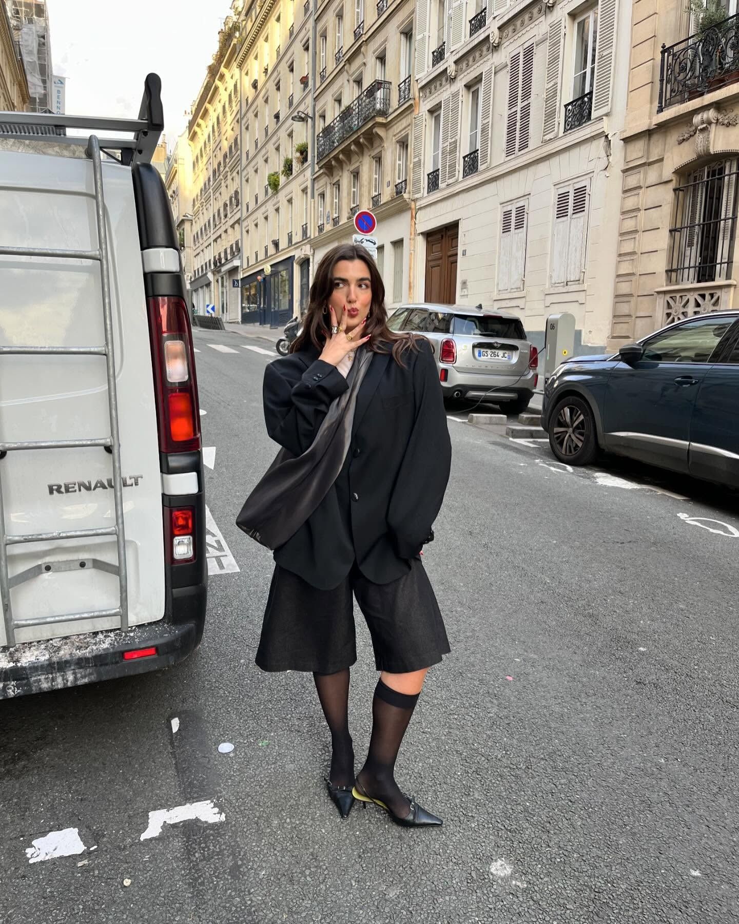 Fashion person Pauline Leroy wears black mesh knee-high socks. She pairs them with black bermuda shorts and a black blazer in a recent image from her Instagram.