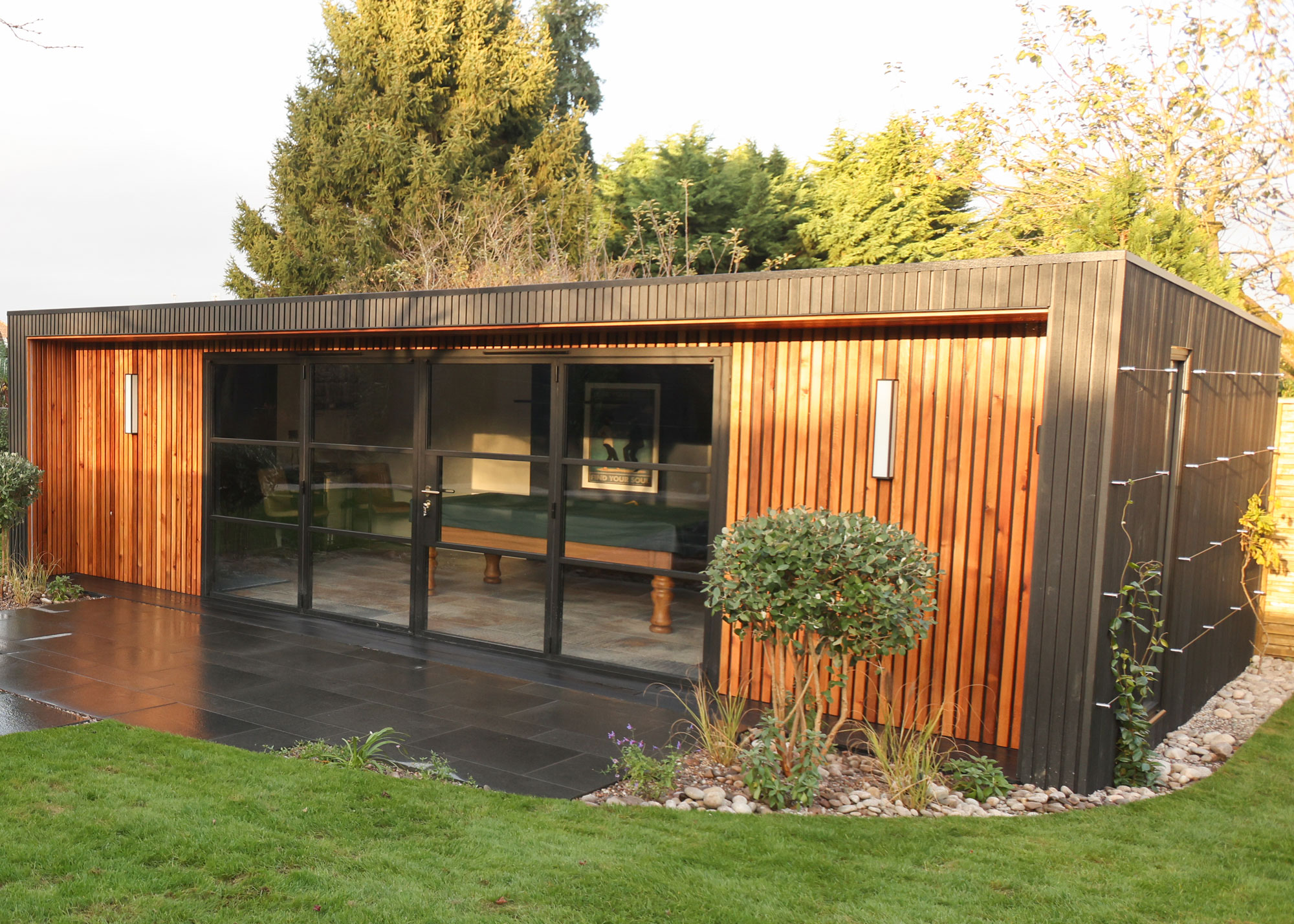 garden room with wooden cladding and glass doors with a pool table visible inside.