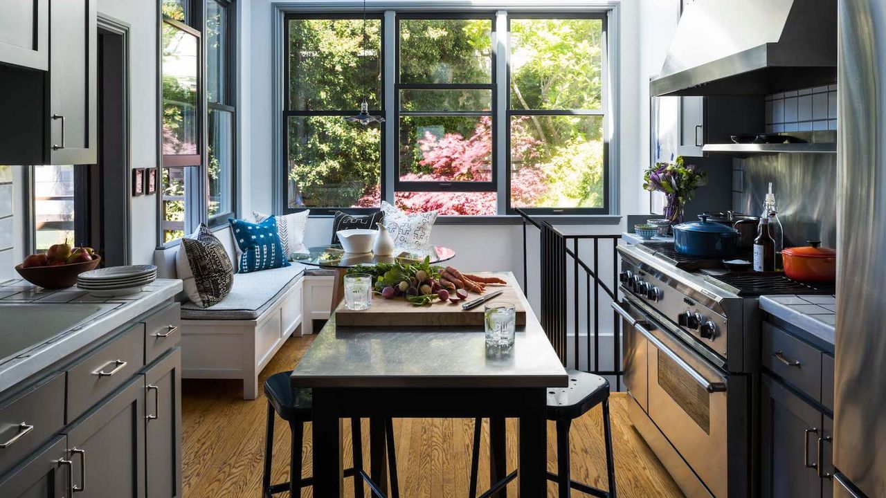 small gray kitchen with large window and small island and bench seating in the corner