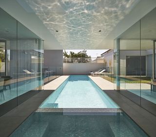 A view of an outdoor swimming pool (partly covered by a ceiling and partly in the open) with sun loungers