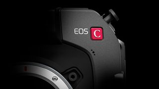 Teaser for a new Canon camera, depicting the top-right corner of a camera body with the red Cinema EOS "C" logo and part of the lens mount, obscured in shadow against a black background